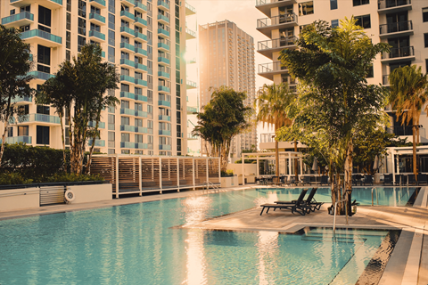 A swimming pool surrounded by trees and chairs in front of apartment buildings.