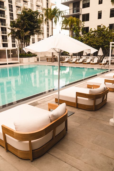 A poolside lounge area with white cushioned seating and a white umbrella.