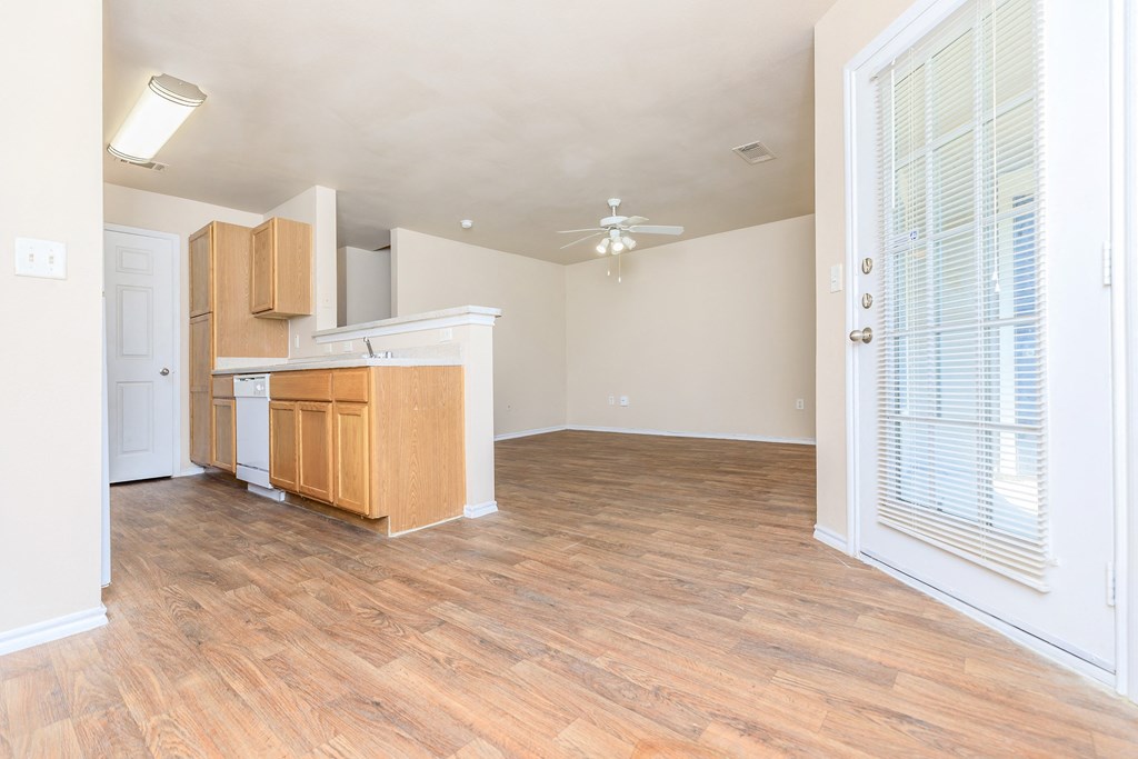 an empty living room with a kitchen and a ceiling fan