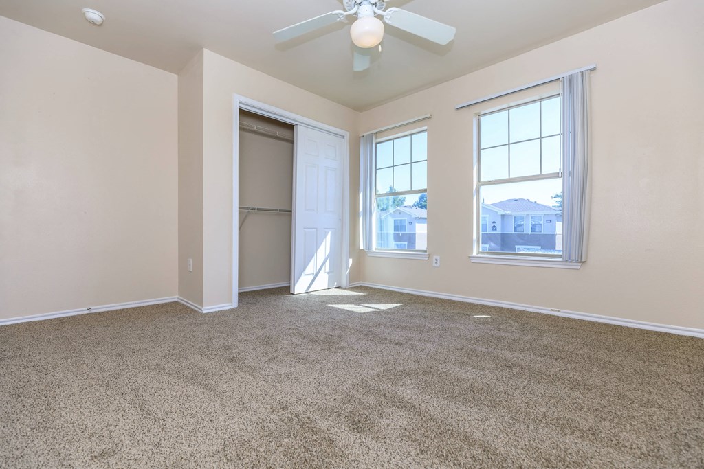 an empty living room with a ceiling fan and two windows