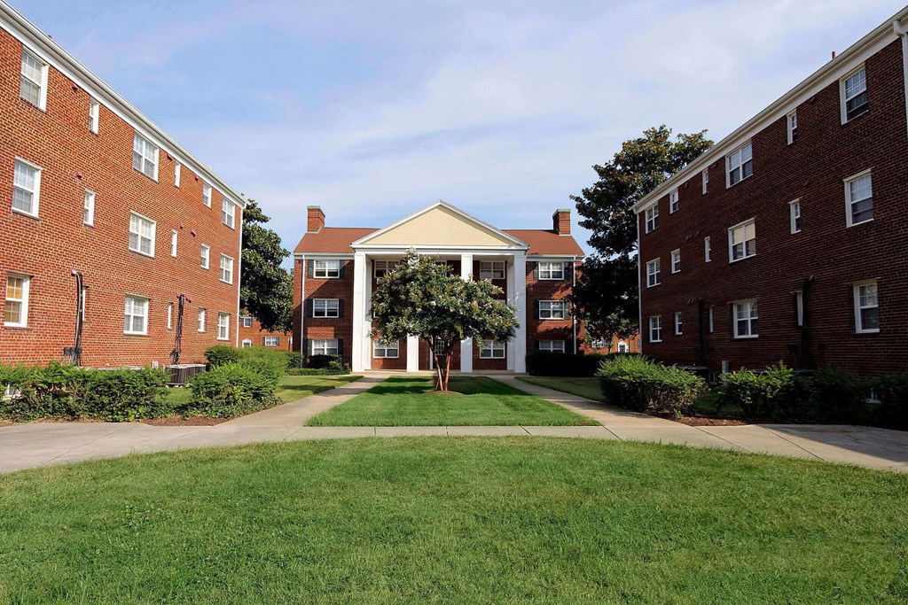 a grassy area with a tree in the middle of it in front of two brick buildings at Parkland Village, Forestville, MD
