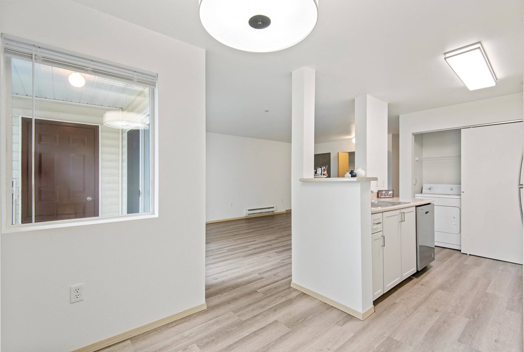a renovated living room and kitchen with white walls and wood flooring