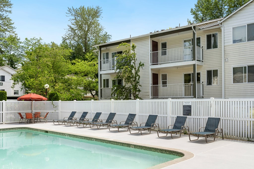 a swimming pool with chairs in front of a house