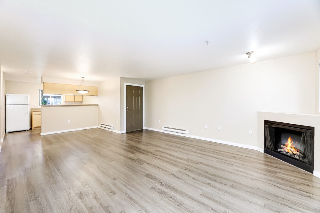 an empty living room with a fireplace and a kitchen