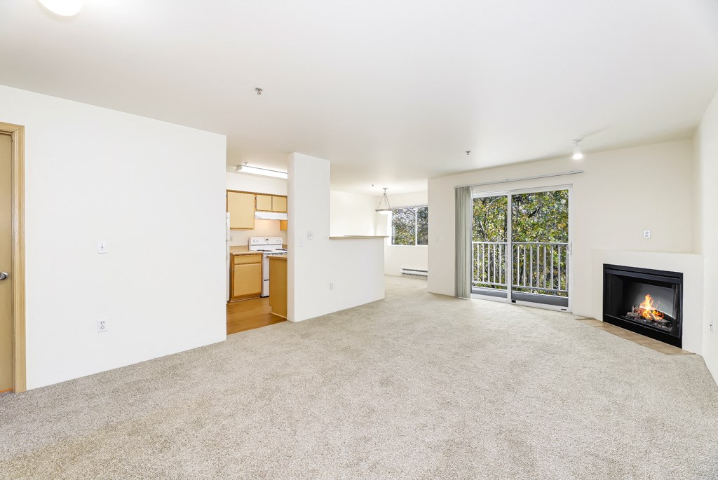an empty living room with a fireplace and a kitchen