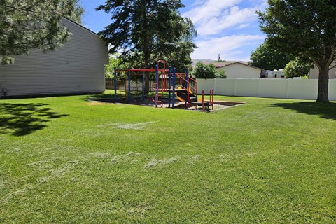 A playground with a red swing set in a grassy area.