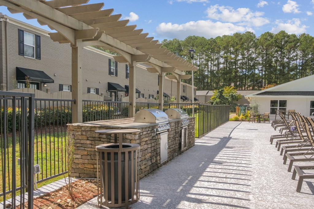 A sunny day at the outdoor seating area of a building with a row of chairs and a trash can.