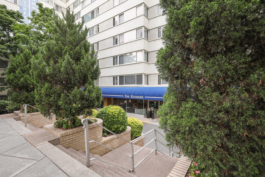 A view of a building with a blue awning and a tree in front of it.
