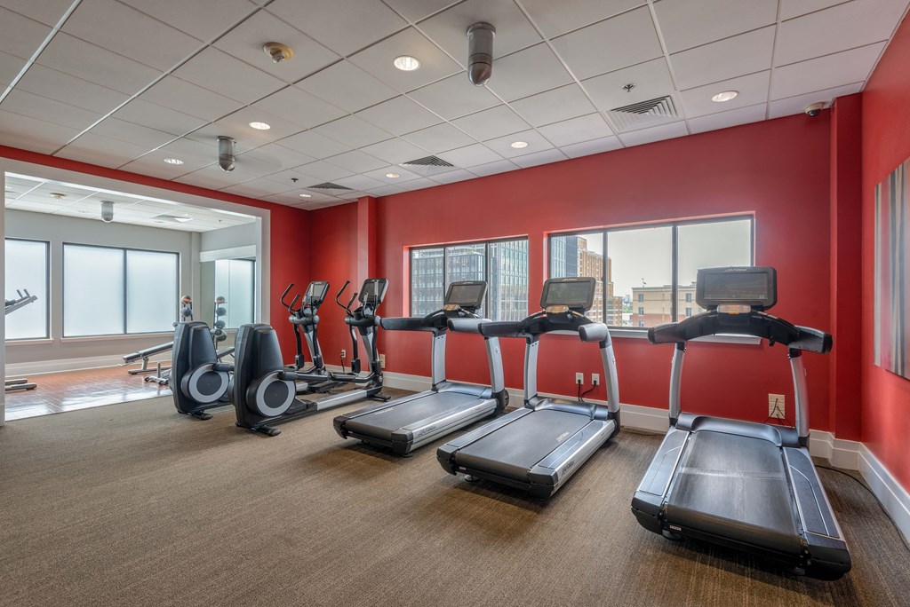 a gym with cardio equipment and red walls and windows