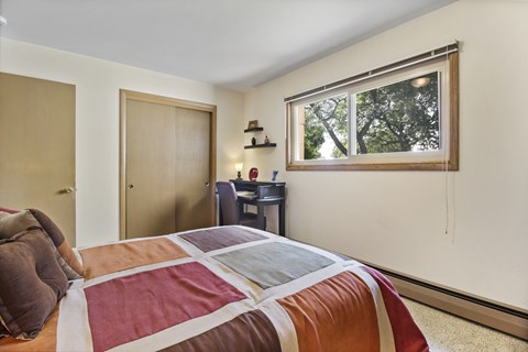 A bedroom with a bed, desk, and window.