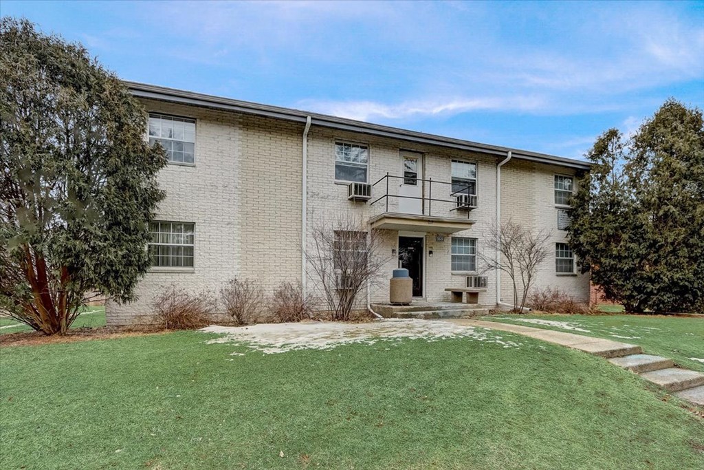 the front of a brick house with a green lawn and a porch
