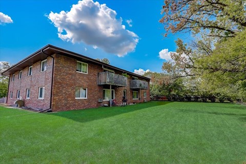 a red brick house with a green lawn and trees