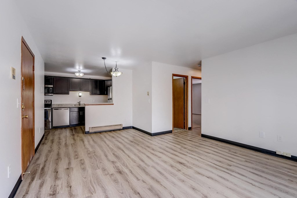 an empty living room with a kitchen in the background