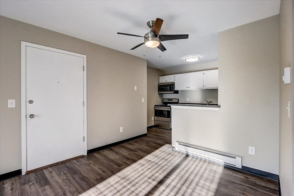 an empty living room with a ceiling fan and a kitchen