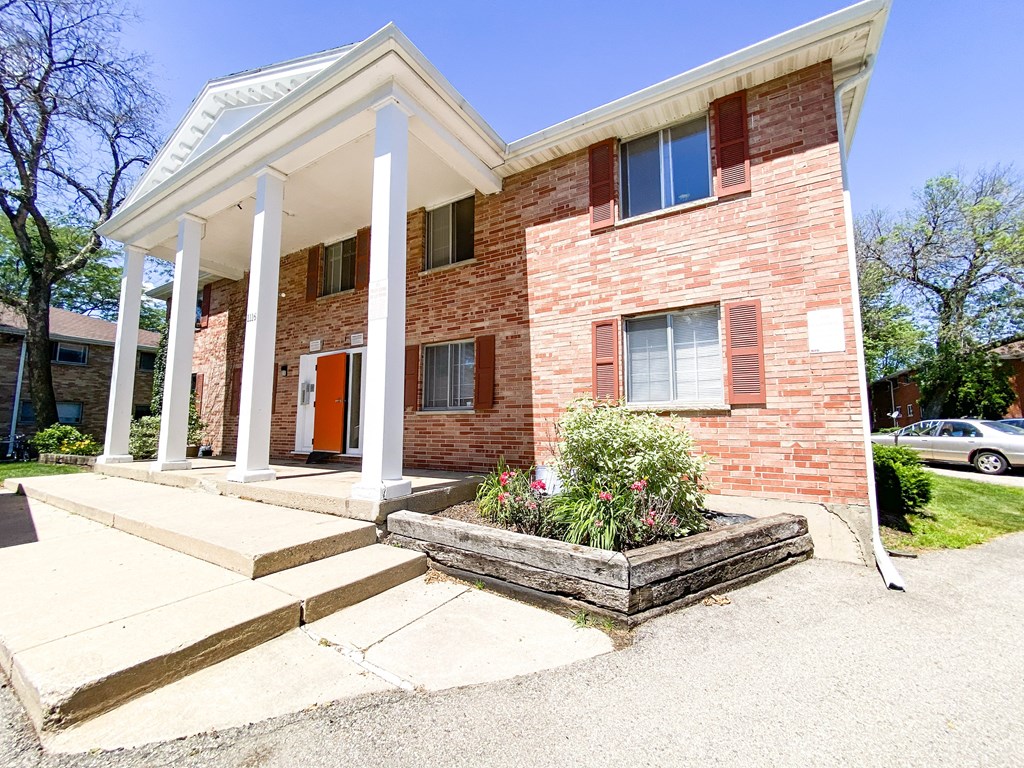 the front of a brick house with white pillars and a porch