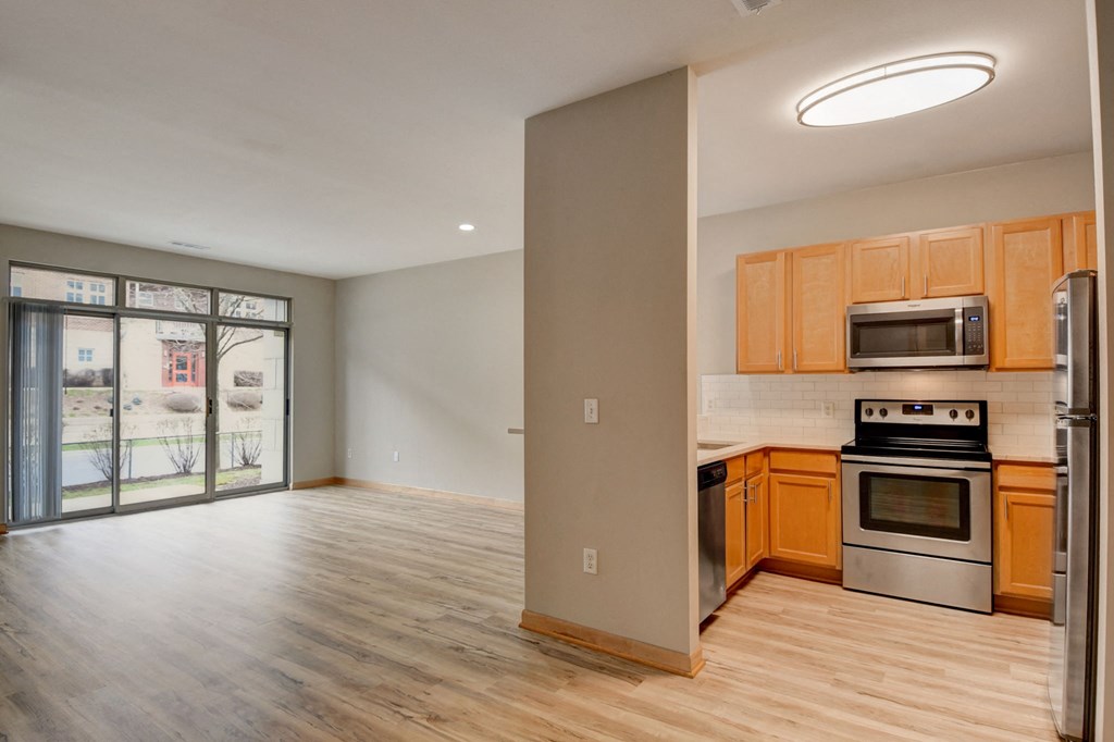 an empty kitchen and living room with wood flooring and a door to a balcony