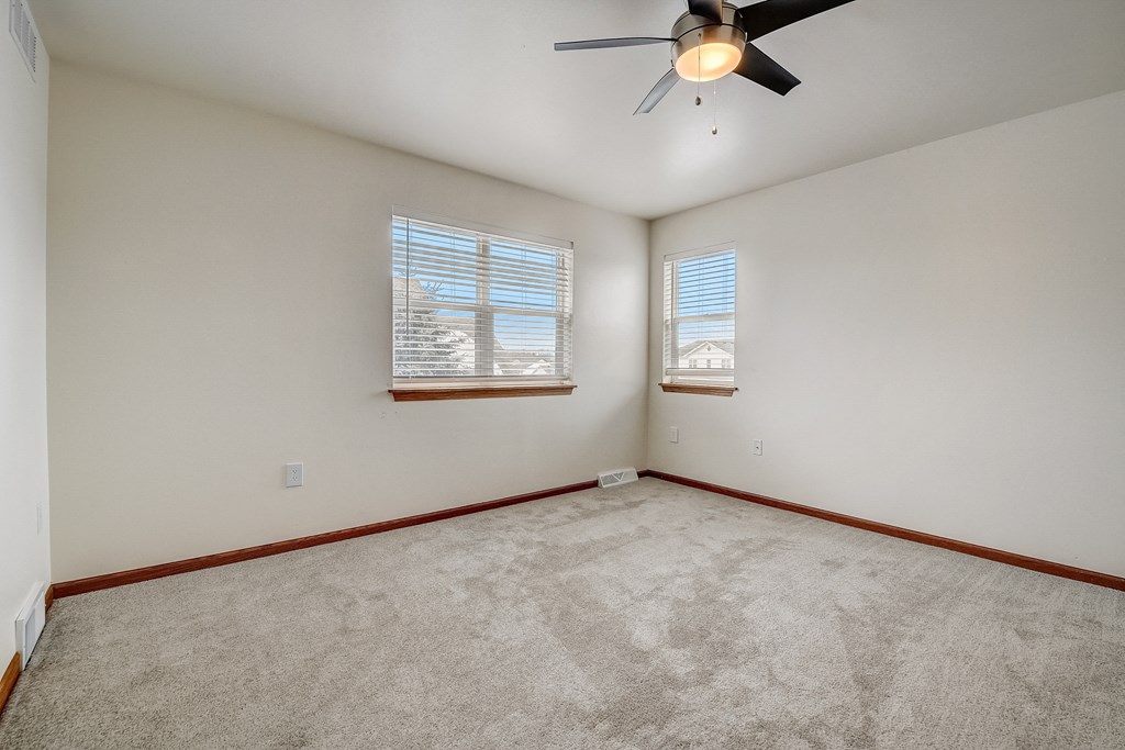 an empty living room with a ceiling fan and two windows