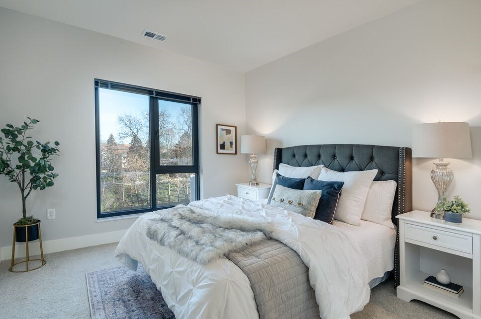 A bedroom with a large bed, a nightstand, and a window with a view of trees.