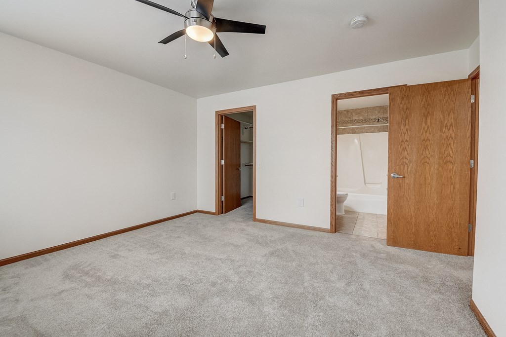 an empty living room with a ceiling fan and a door to a bathroom