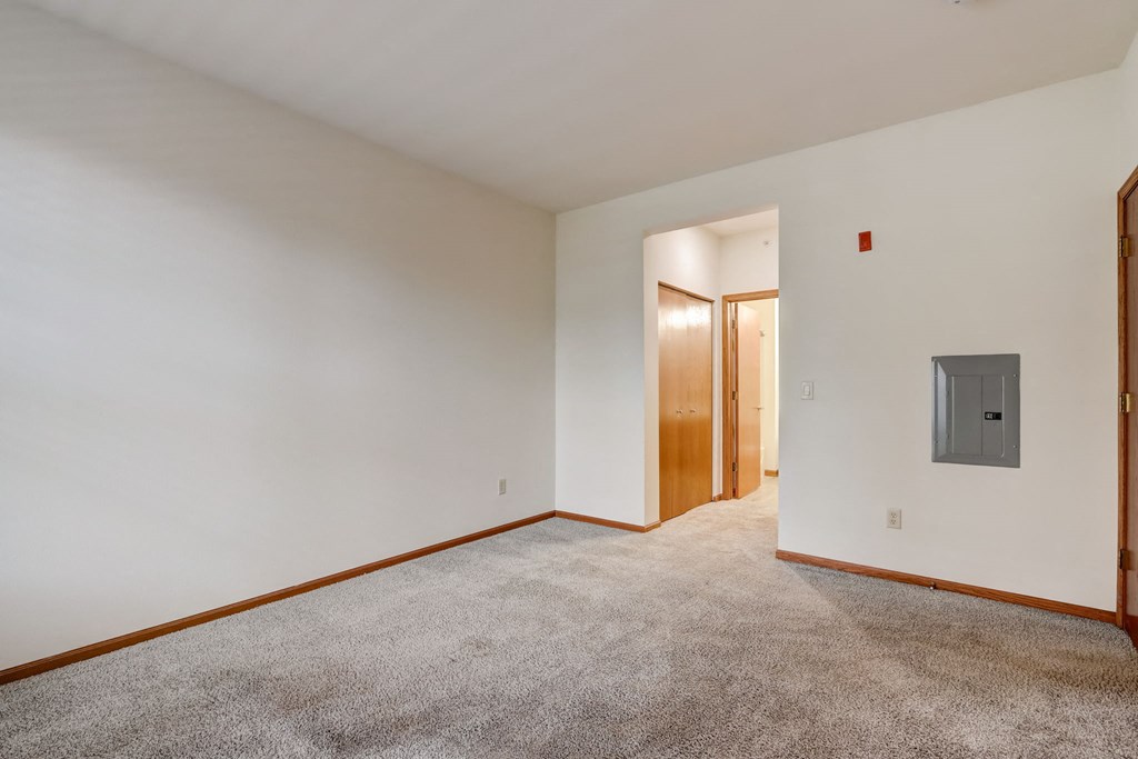 a living room with white walls and carpet and a door to a hallway