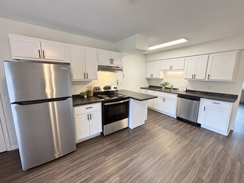 A modern kitchen with a stainless steel refrigerator and wooden flooring.
