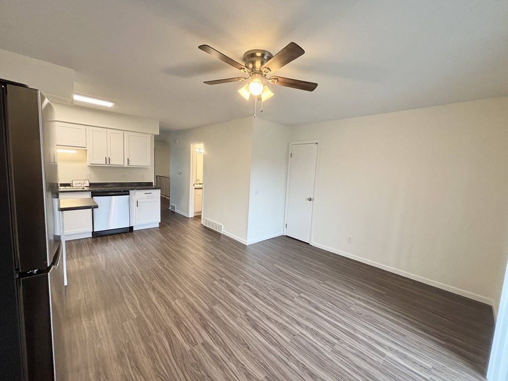 A room with a ceiling fan and a kitchen area with a refrigerator.