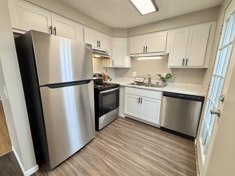 A kitchen with a stainless steel refrigerator and wooden flooring.