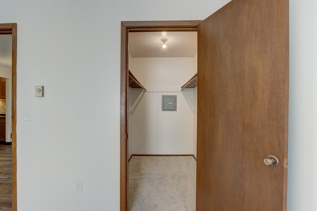 a walk in closet in a bedroom with white walls and a wooden door