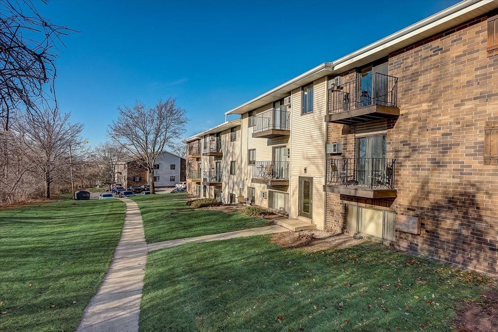 a brick apartment building with green grass and a sidewalk