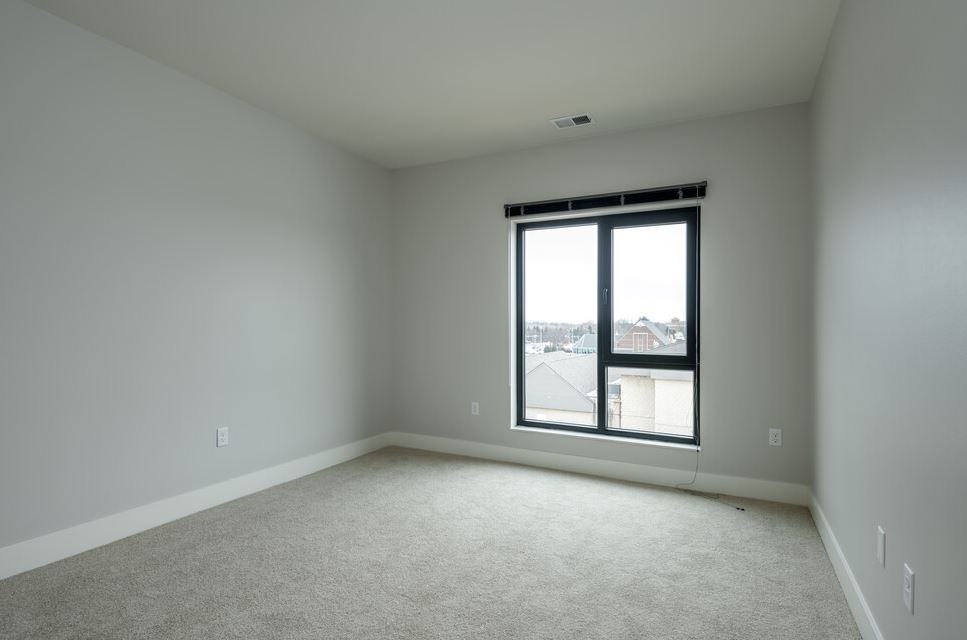 A room with a carpeted floor and a window showing a view of buildings outside.