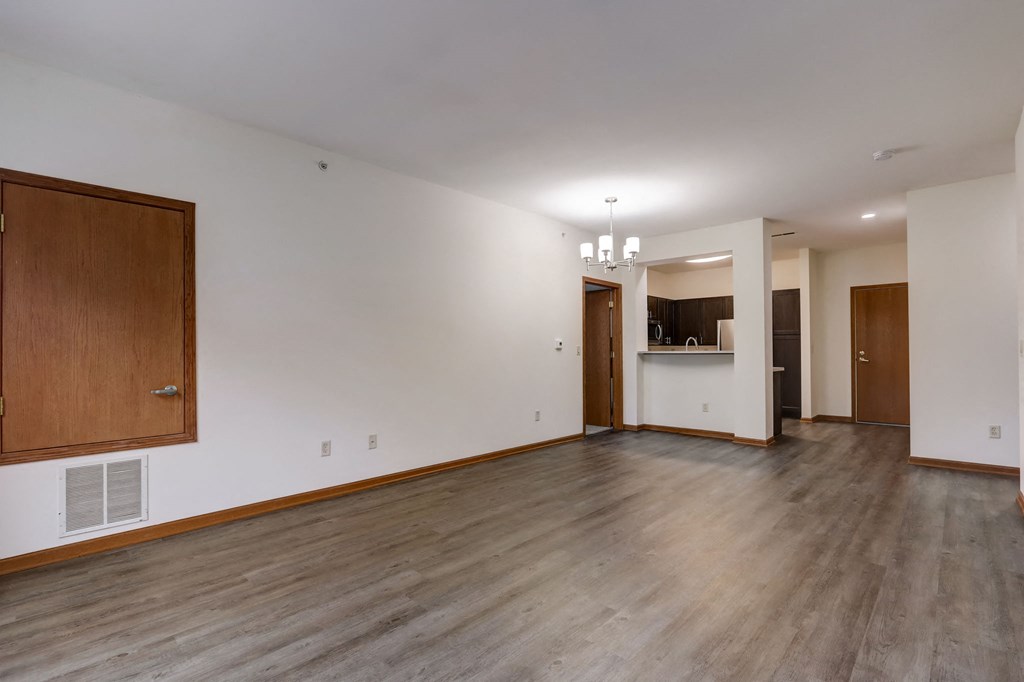an empty living room with wood floors and white walls and a kitchen