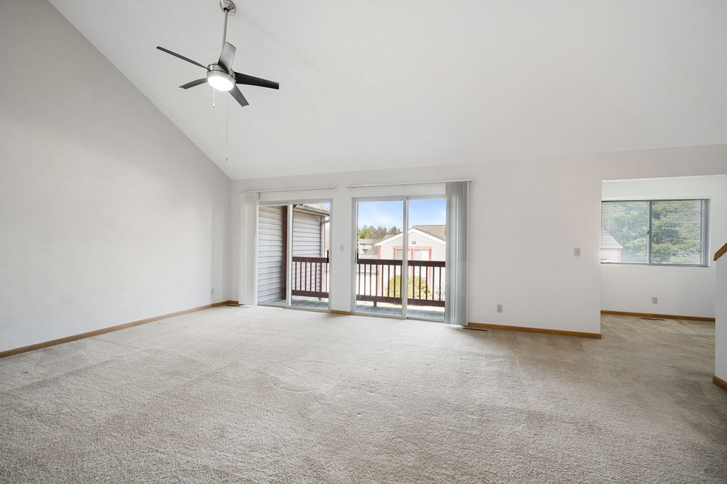 an empty living room with a ceiling fan and a balcony