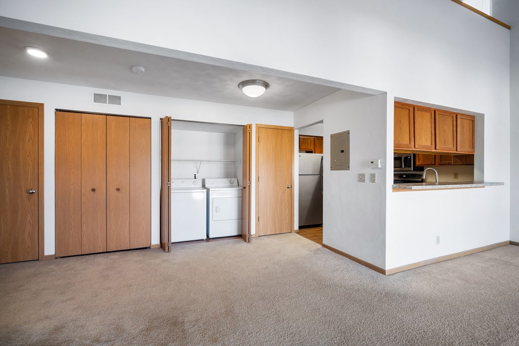 an empty living room with a kitchen with a refrigerator and a sink