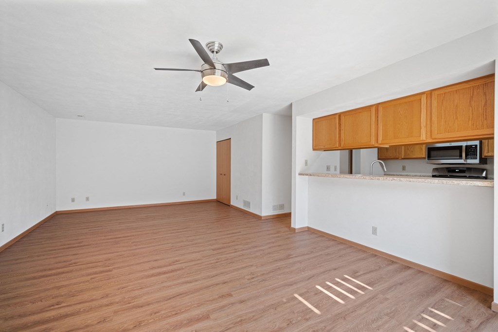 an empty living room with a ceiling fan and a kitchen