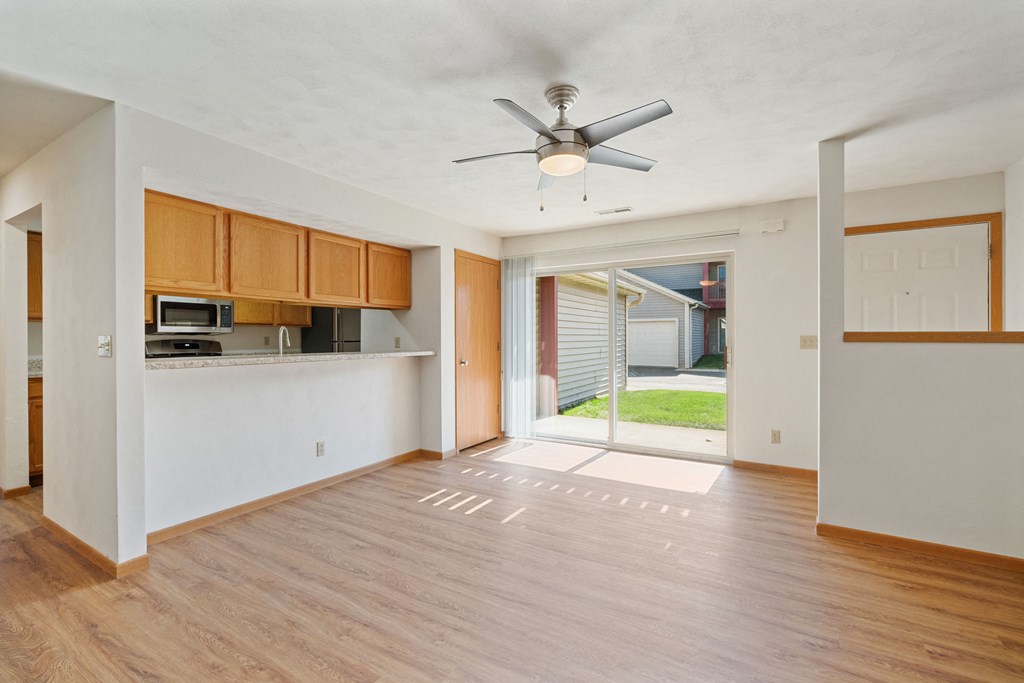 an empty living room with a ceiling fan and a kitchen