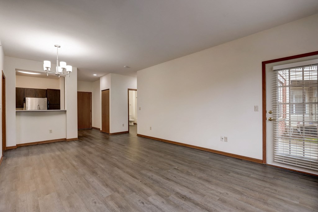 the living room and kitchen of an empty house with wood floors and a large window