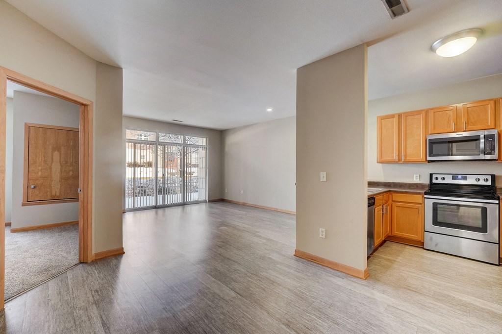 an empty living room and kitchen with wood flooring and stainless steel appliances
