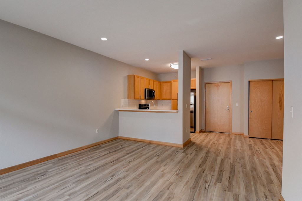 an empty living room with wood flooring and a kitchen