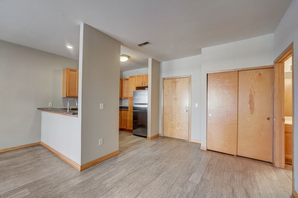 the living room and kitchen of an empty apartment with wood flooring and white walls