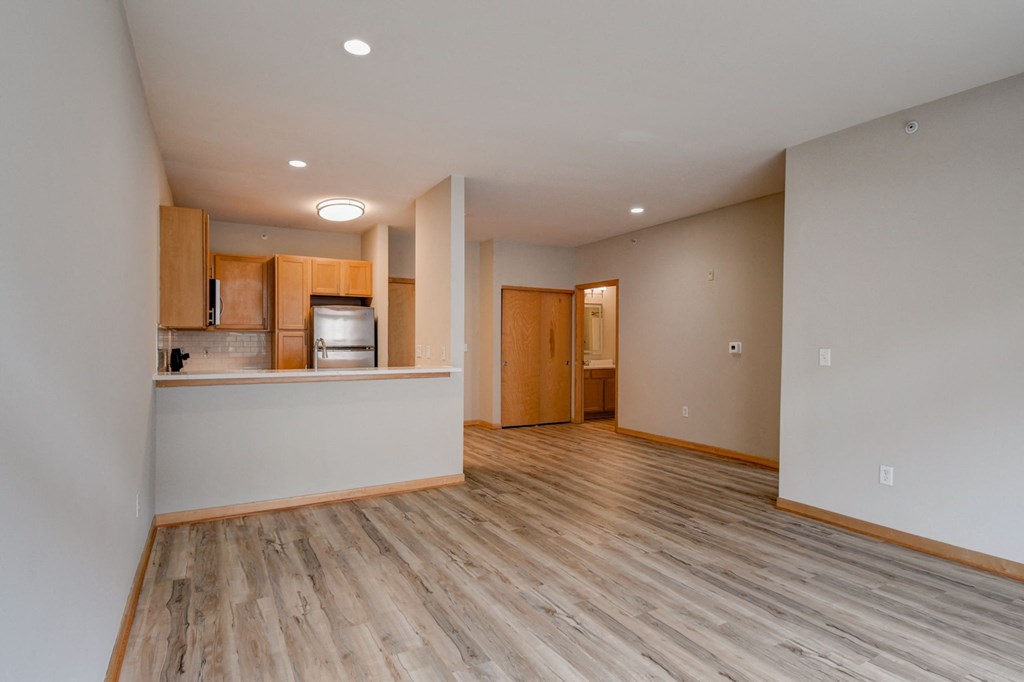 an empty living room with wood flooring and a kitchen