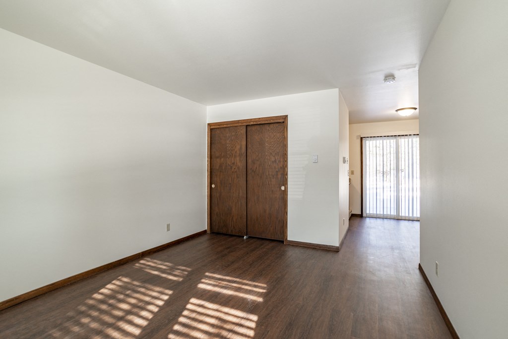 a living room with white walls and wood floors and a wooden door