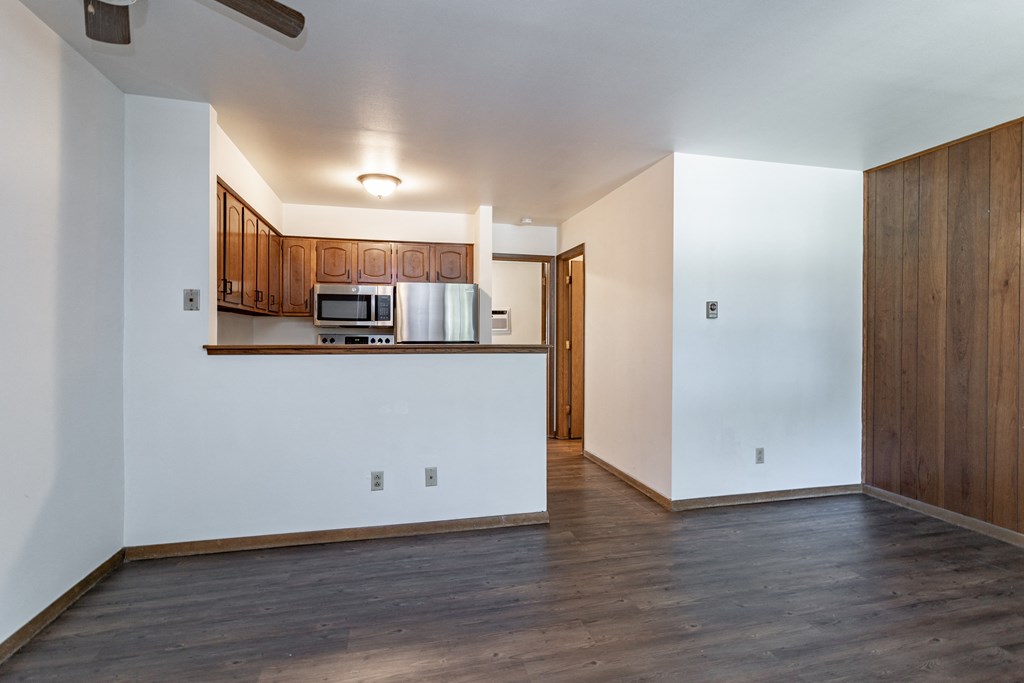 an empty living room with wood floors and white walls and a kitchen