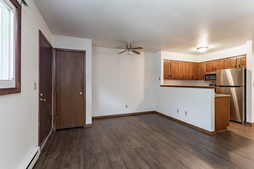 an empty living room with a kitchen and a ceiling fan