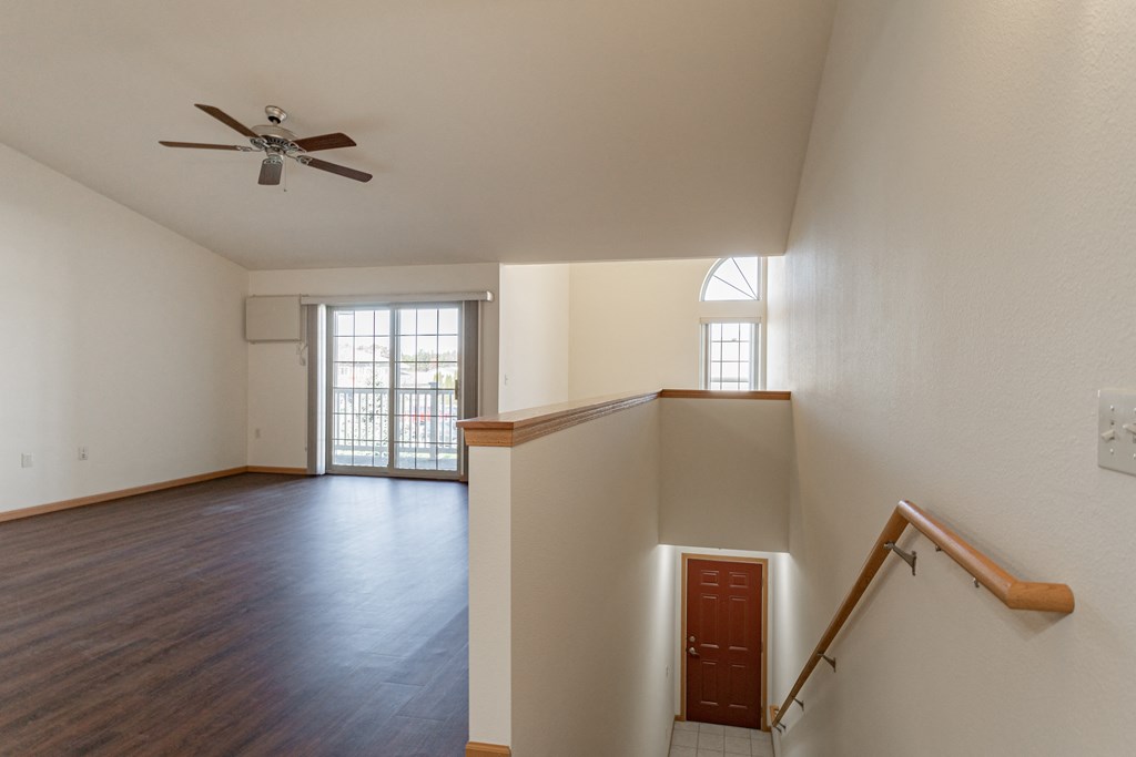 an empty living room with a staircase and a ceiling fan