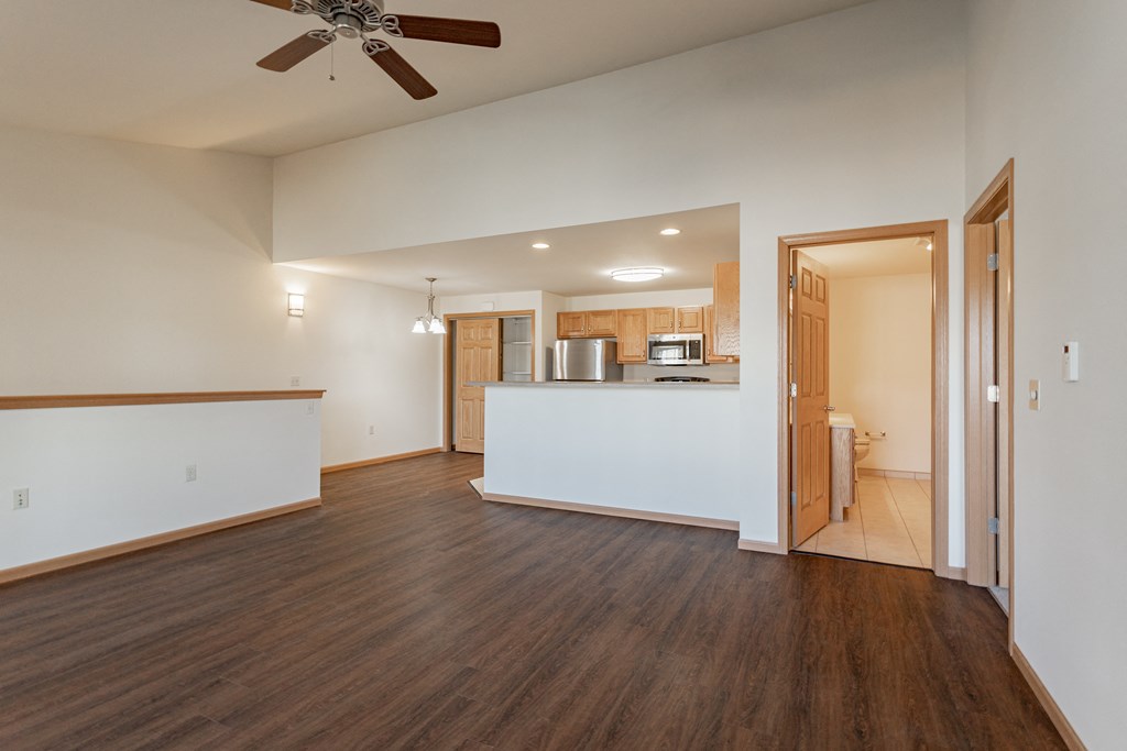 an empty living room with a kitchen and a ceiling fan