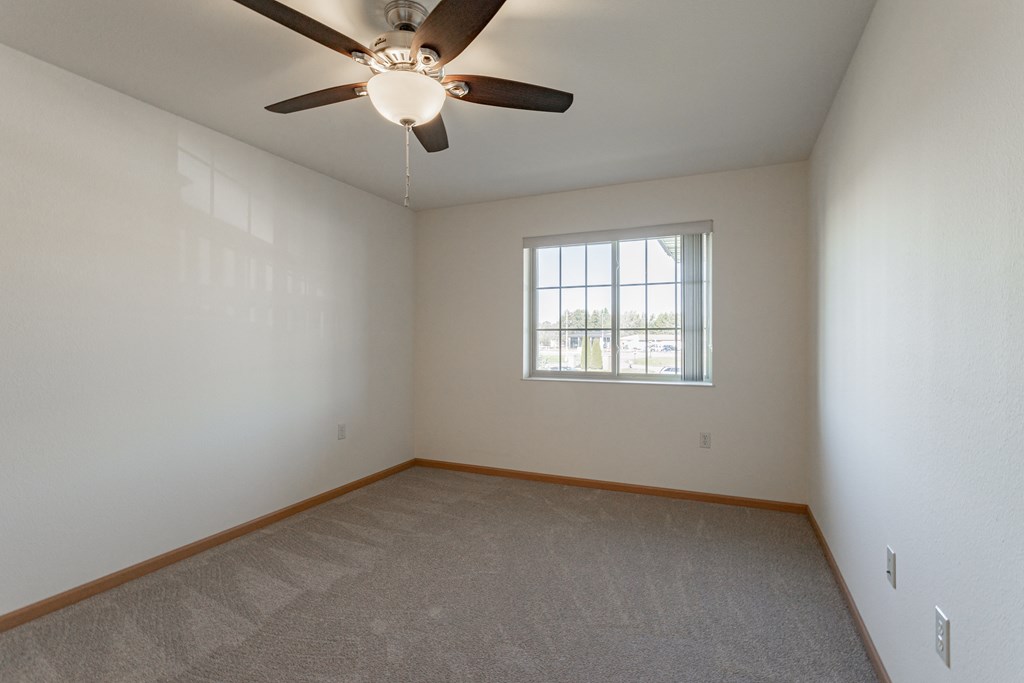 an empty living room with a ceiling fan and a window