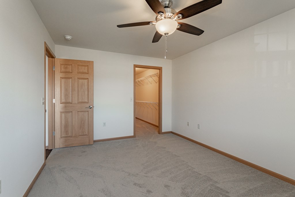 an empty living room with a ceiling fan and a door to a bedroom
