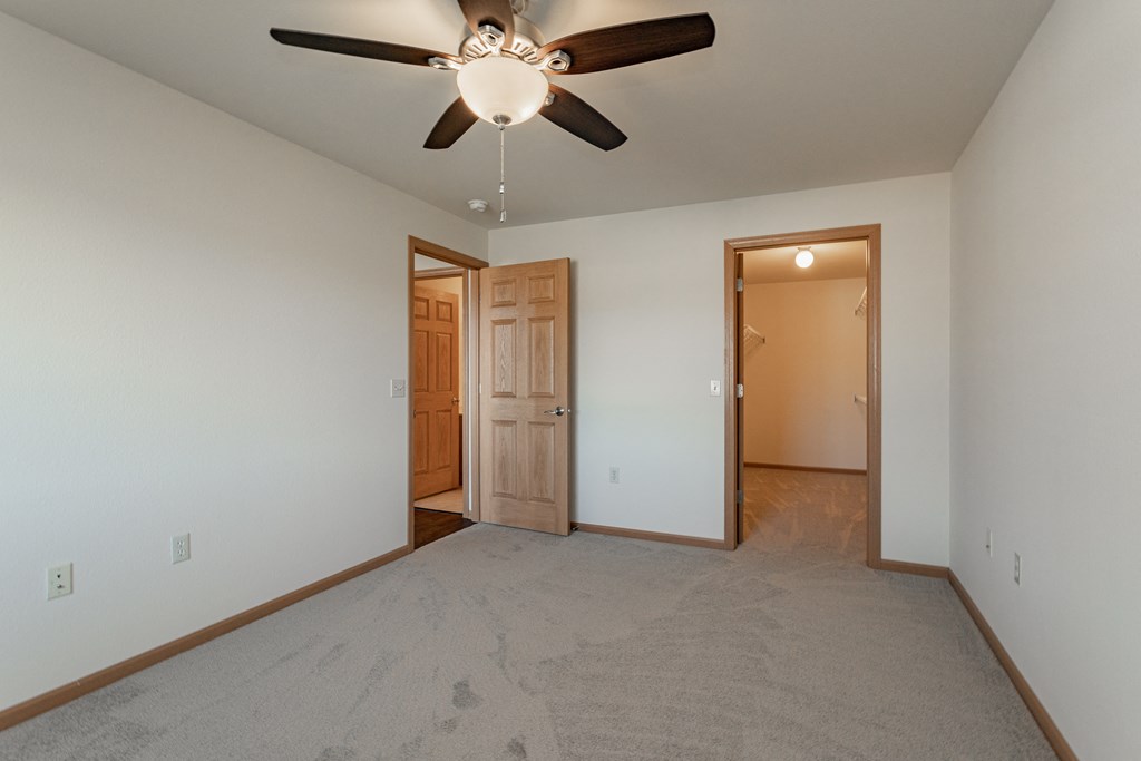an empty living room with a ceiling fan and a door to a bedroom