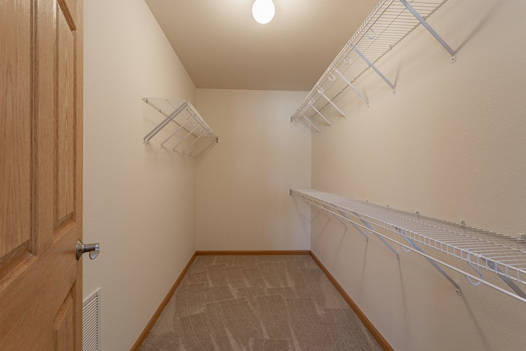 the walk in closet has a lot of shelves and hooks for clothes