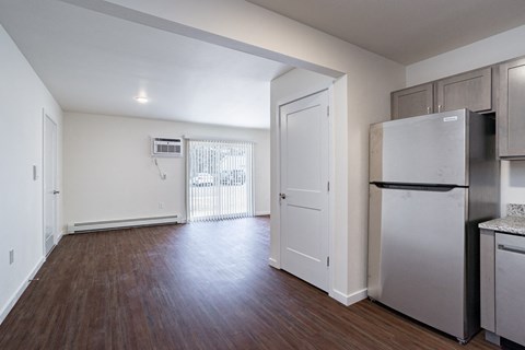 an empty living room with a refrigerator and a door into a kitchen